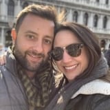 Homem e mulher sorrindo para a câmera, posando juntos ao ar livre com prédios históricos ao fundo