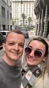 Duas pessoas tirando selfie na rua urbana com prédios altos ao fundo