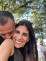 Homem beijando mulher sorrindo ao ar livre com árvores e vegetação ao fundo