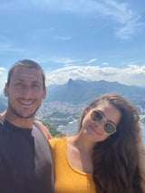 Casal sorrindo para a câmera com paisagem de montanha e cidade ao fundo